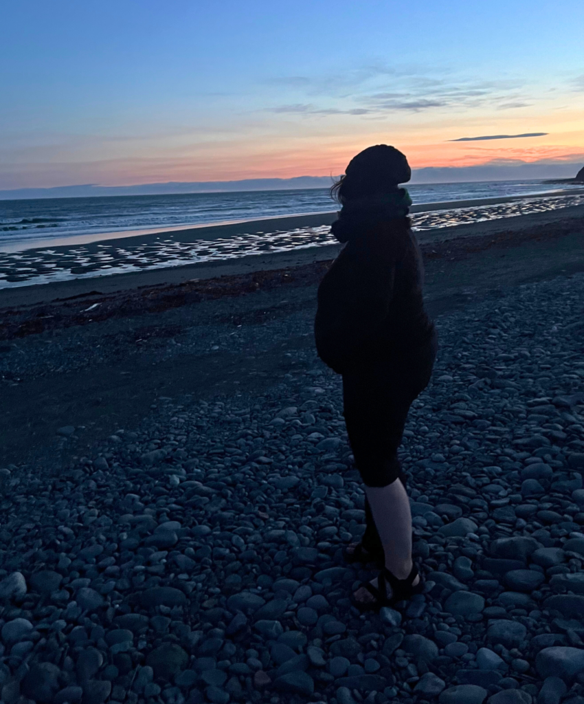 Person looks out at a sunset behind the mountains across the ocean